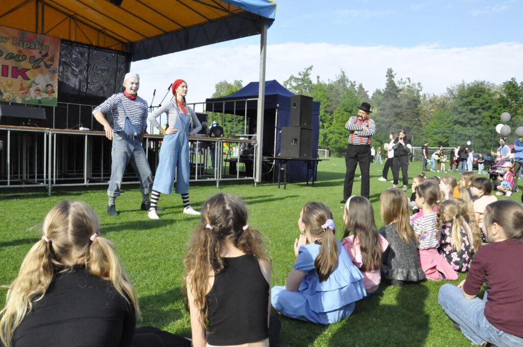 Troje mimów stoi na boisku. Przed nimi na trawie siedzą dzieci. pogodny dzień.
