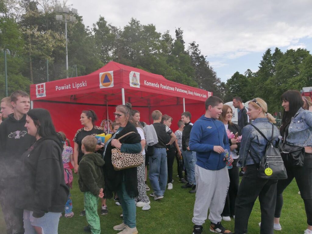 Dorośli i młodzież stoją przy czerwonym namiocie Komendy Powiatowej Państwowej Straży Pożarnej.