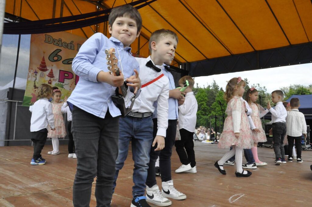 Dzieci n scenie plenerowej. W pierwszym planie chłopiec trzymający gitarę.
