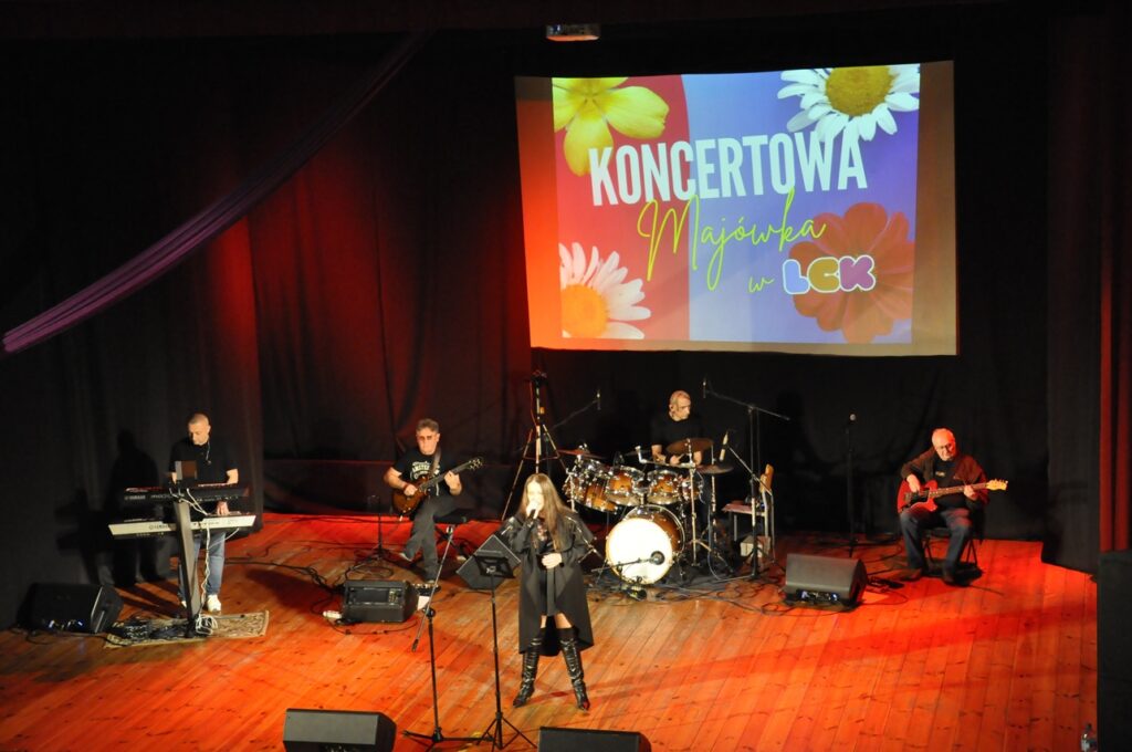 Grupa muzyków na scenie. Nad nimi wyświetlany baner wydarzenia.