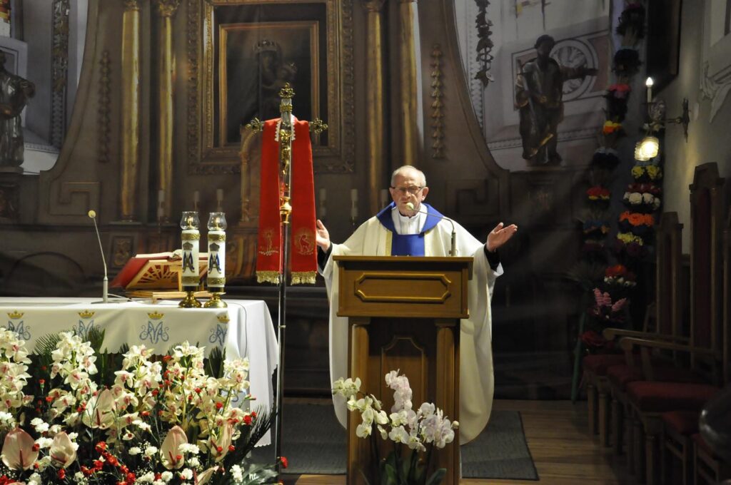 Ołtarz kościelny. Ksiądz Wznosi ręce. Ciepłe oświetlenie.