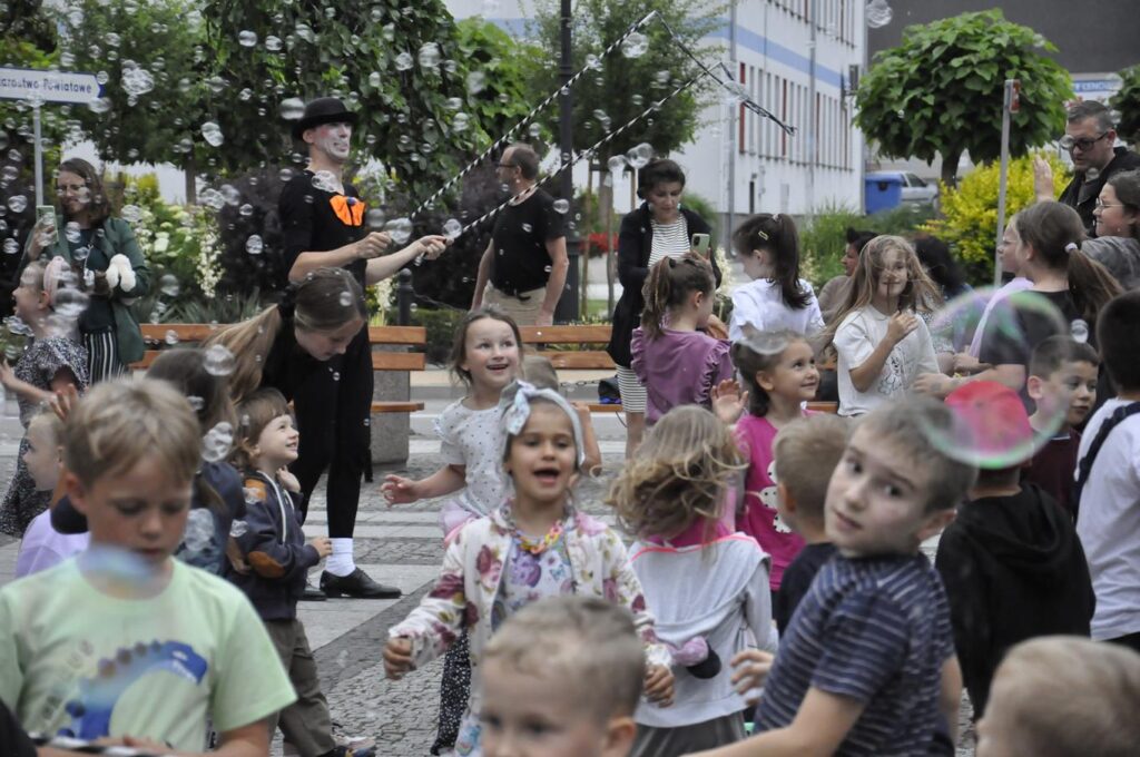 Duża grupa uśmiechniętych dzieci i dorosłych. Wokół szybują bańki mydlane.