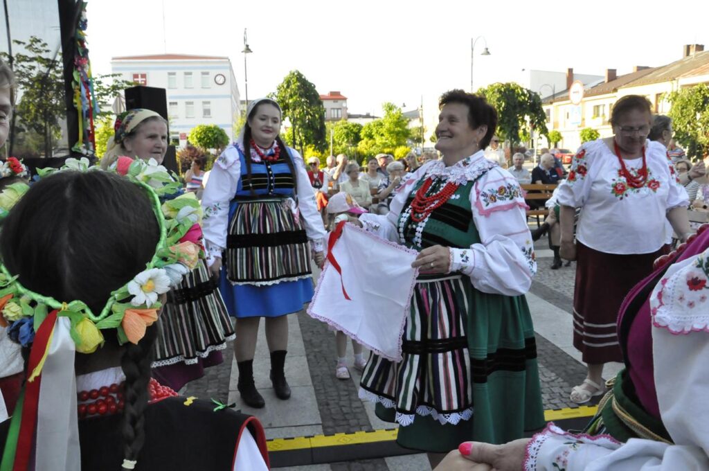 Ludzie w ludowych strojach tańczą. W tle zieleń parku. pogodny dzień.