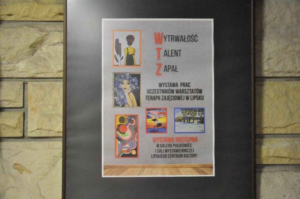 Plakat promujący wystawę w antyramie z czarnym tłem na ścianie z płyt piaskowca.