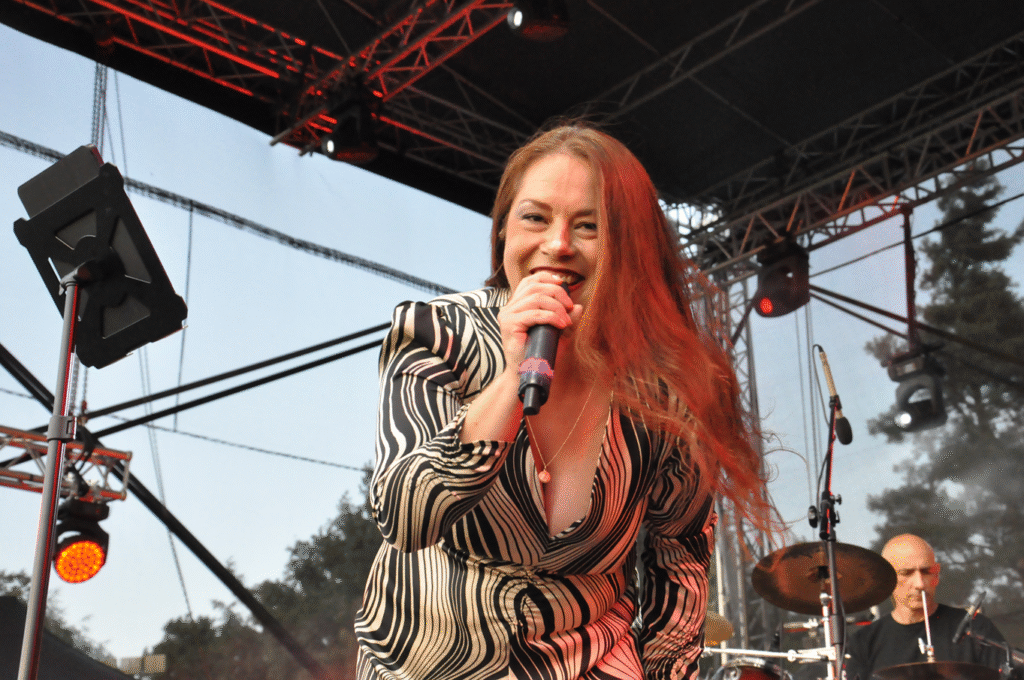 Kobieta z długimi włosami i czarno-białej sukience w fale trzyma mikrofon przy ustach.