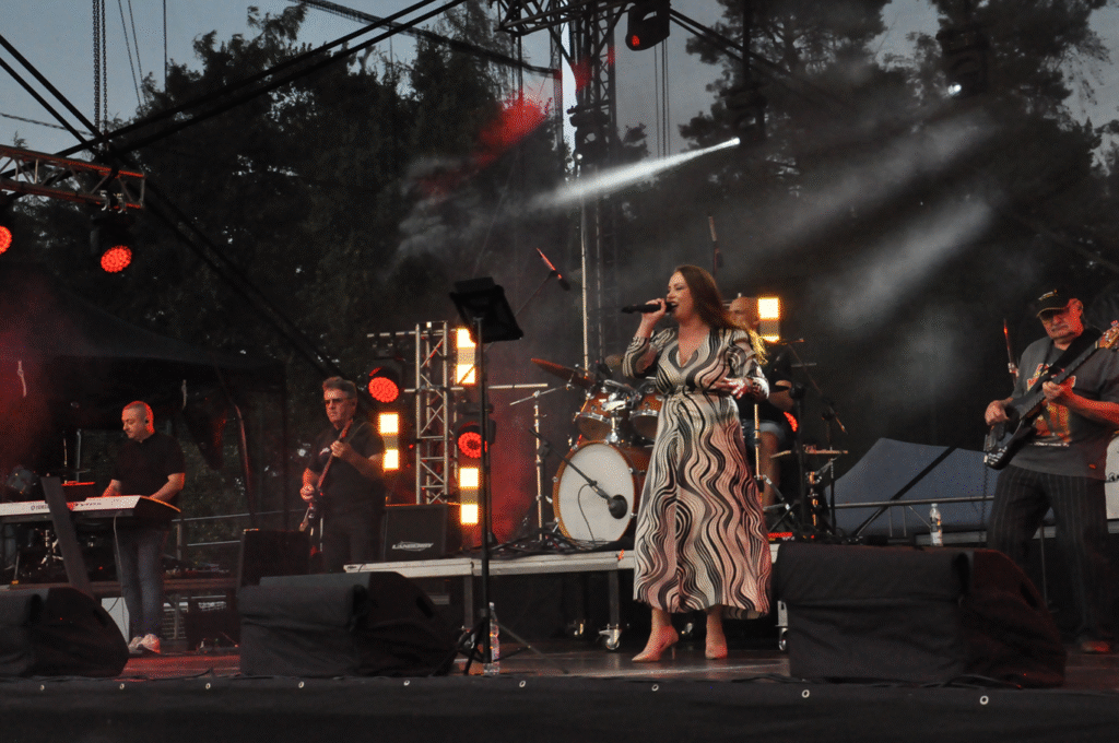 Muzycy i wokalistka w sukience w czarno-białe fale koncertują na scenie. Półcień.