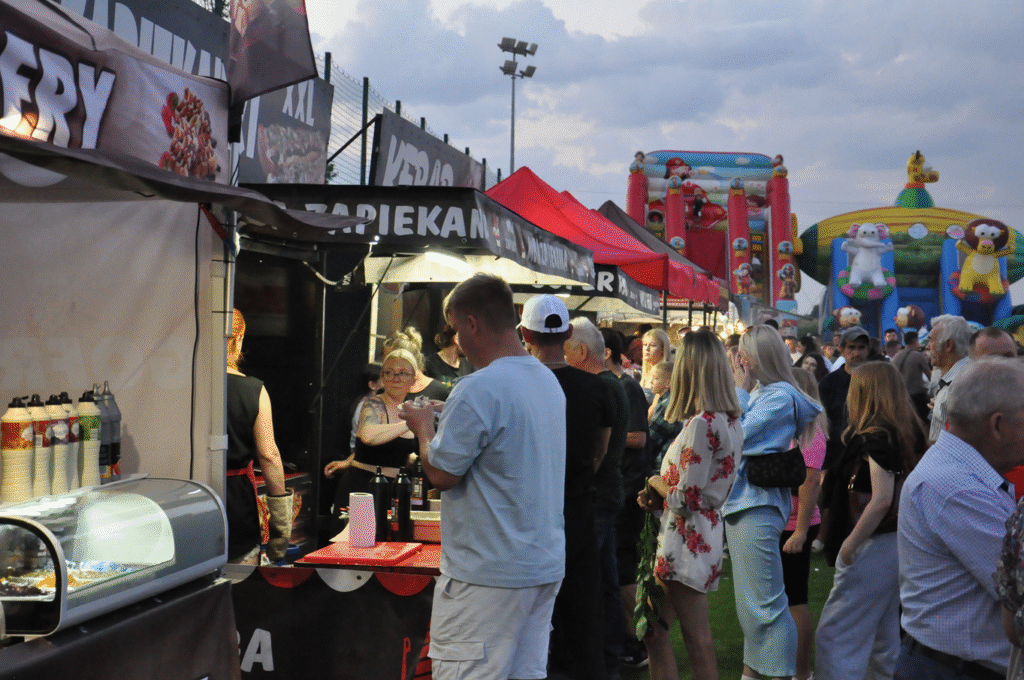 Altanki z atrakcjami festynowymi. Przed nimi duża grupa spacerujących ludzi.