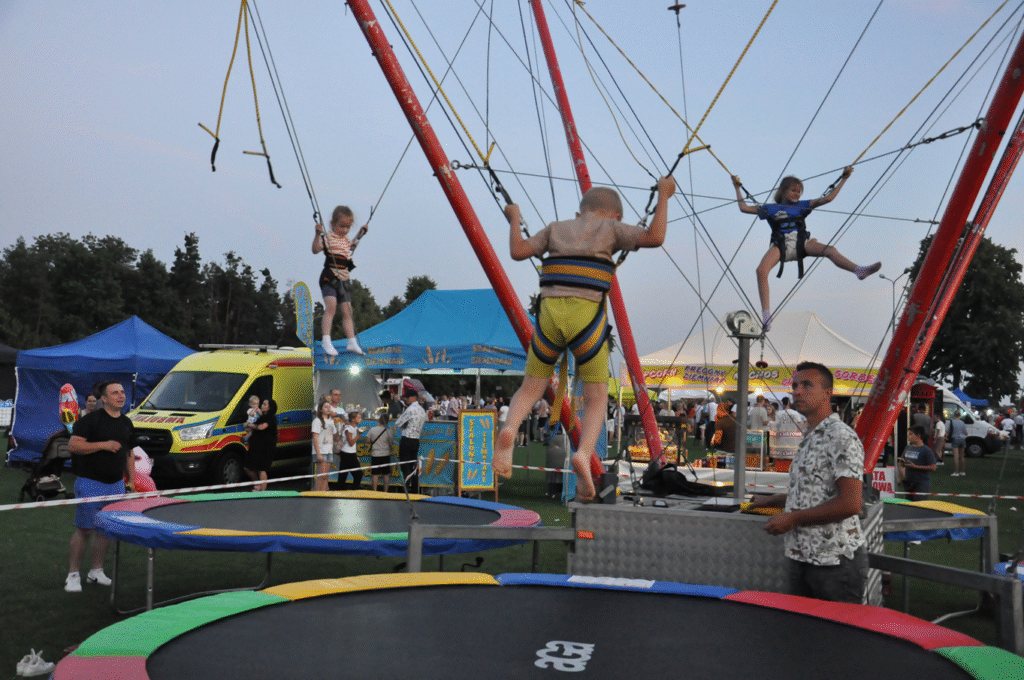 Trójka dzieci skacze na trampolinach z zabezpieczeniem.