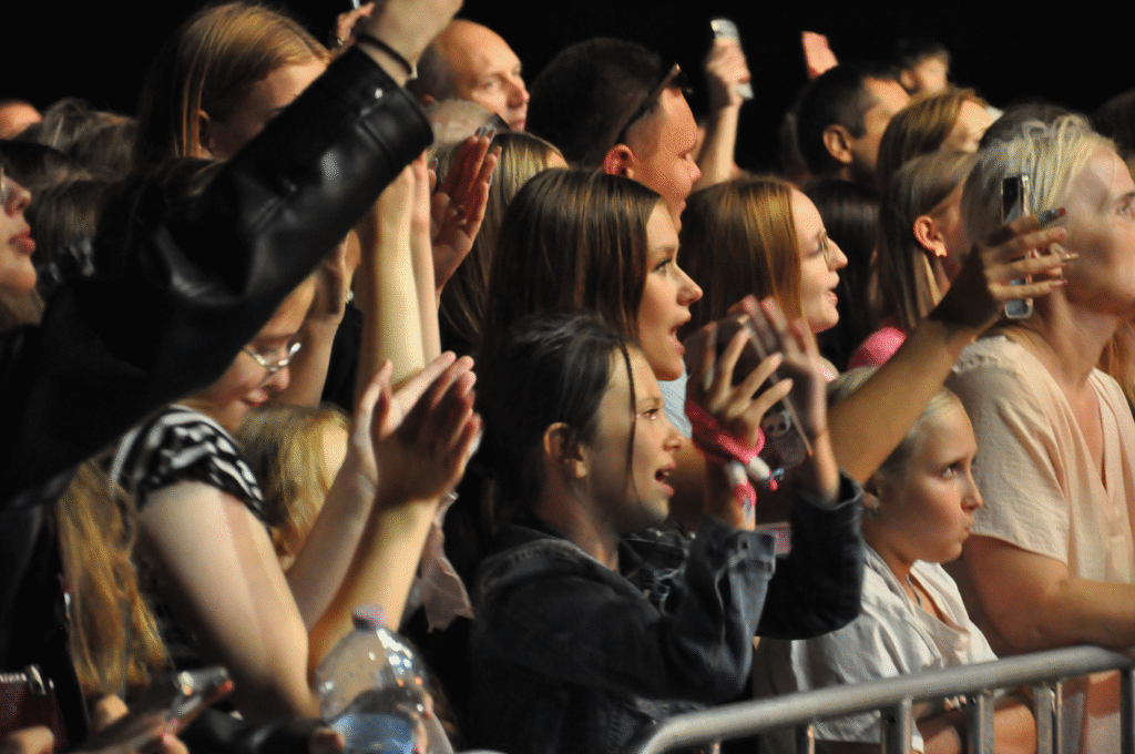 Młode osoby przy barierkach nagrywające telefonami.