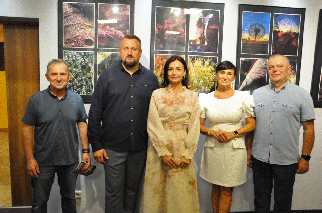 Dwie kobiety i trzech mężczyzn pozuje do wspólnego zdjęcia. Za nimi wiszą antyramy z fotografiami.