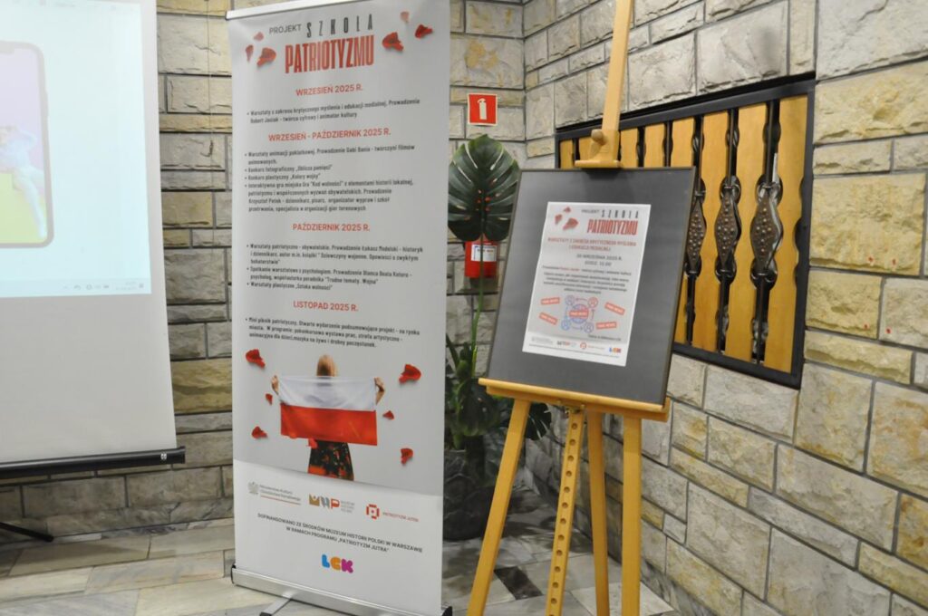 Rollup i stelaż z plakatem. W tle kamienna ściana. Pomieszczenie ciepło oświetlone.