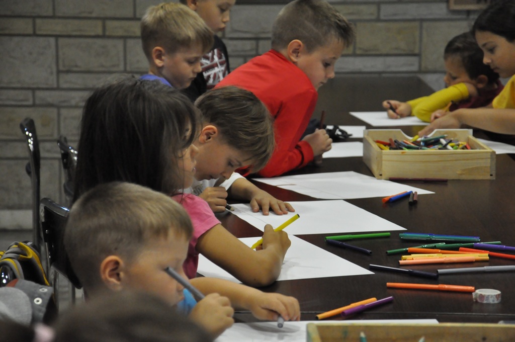 Dzieci siedzą przy stole i wykonują prace plastyczne.