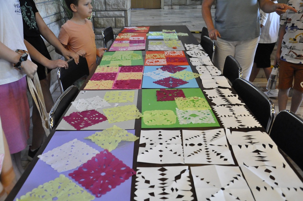 Na stole leżą kolorowe wycinanki. Obok stoi kilka osów.