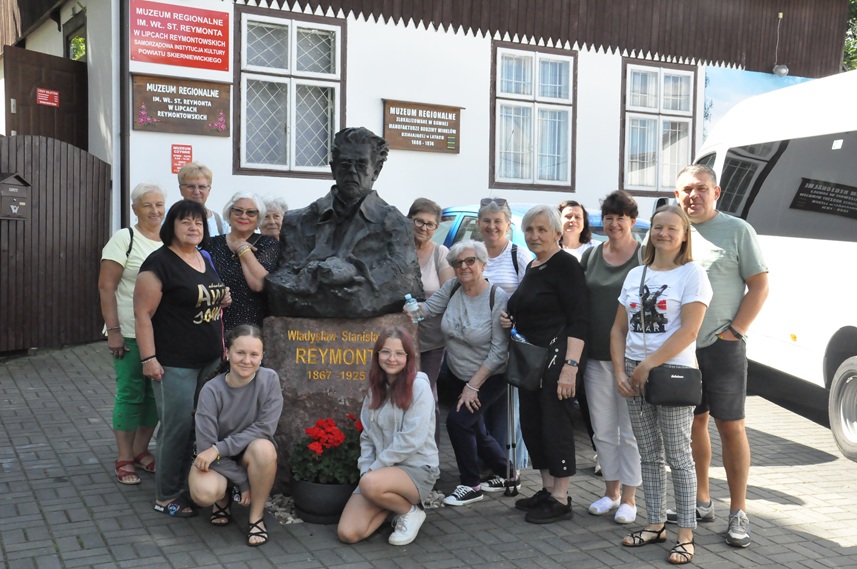 Dorośli i dwie nastolatki pozują do wspólnego zdjęcia przy pomniku Reymonta w Lipcach Reymontowskich.