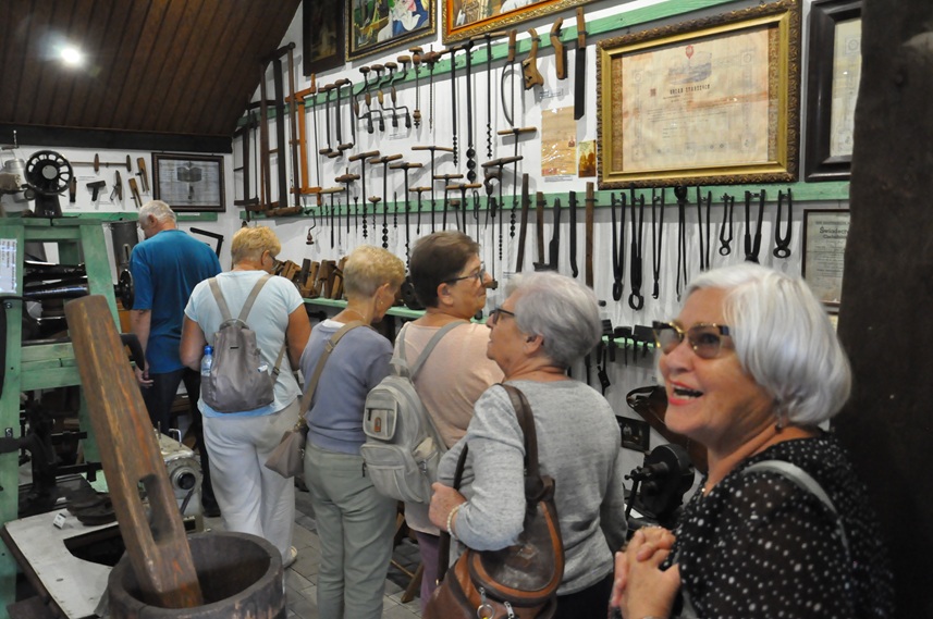 Grupa dorosłych osób ogląda ekspozycję chaty ludowej.