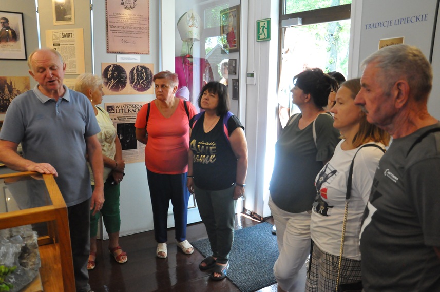 Grupa dorosłych osób ogląda ekspozycję chaty ludowej.