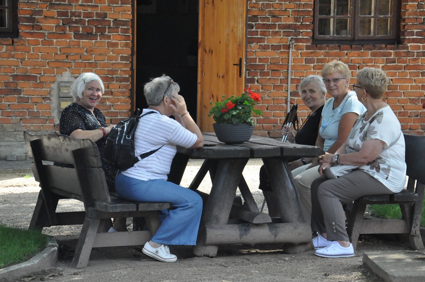 Kilka kobiet siedzi przy stole obok budynku z czerwonej cegły. Pogodny dzień.