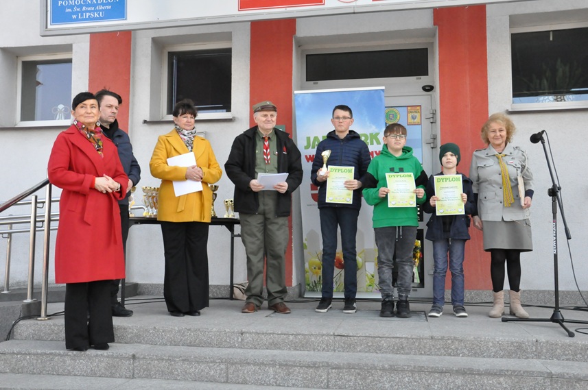 Dzieci i dorośli pozują do wspólnego zdjęcia na schodach. Niektórzy trzymają jasnozielone dyplomy.