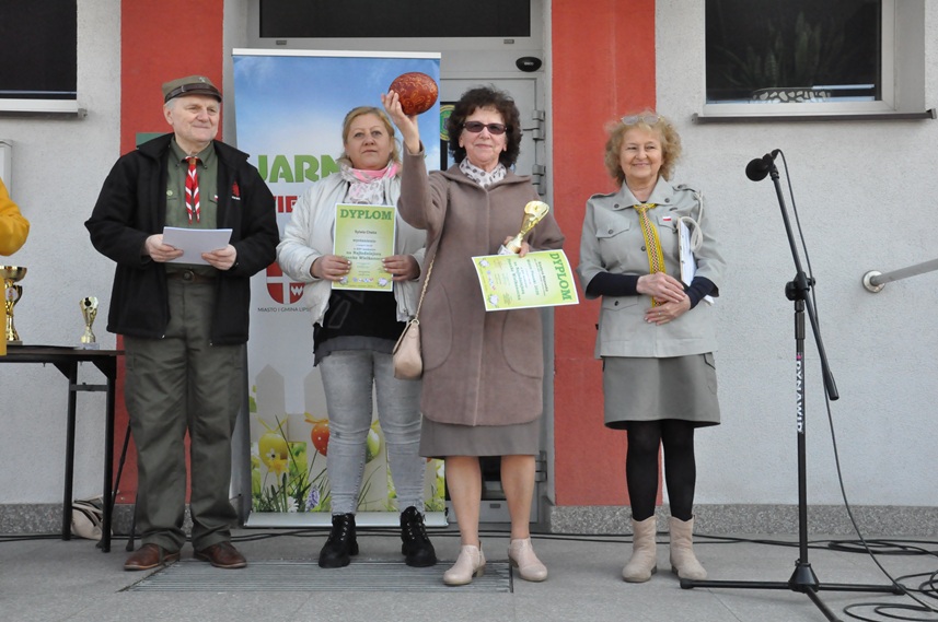 Cztery osoby pozują do wspólnego zdjęcia. Kobieta w czarnych włosach trzyma brązową pisankę i dyplom.