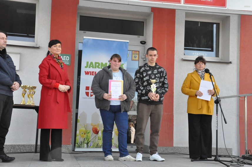 Pięć osób pozuje do wspólnego zdjęcia. Dziewczyna w szarej bluzie trzyma dyplom, a chłopak w czarnej bluzie z białymi nadrukami puchar.