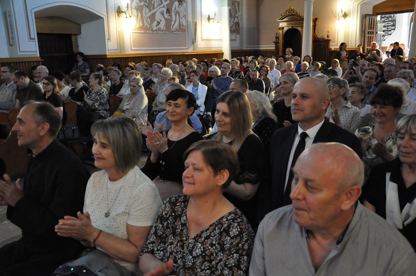 Duża grupa ludzi siedzi w kościelnych ławach. Na ścianach freski ostatniej drogi Jezusa na Golgotę oraz konfesjonał.